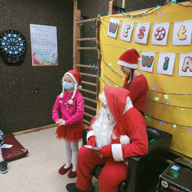 uczeń w przebraniu Św. Mikołaja słucha wierszyka w wykonaniu dziewczynki - podopiecznej Świetlicy Środowiskowej