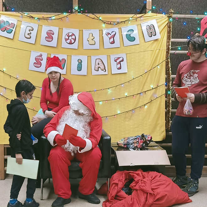 wolontariusz w przebraniu Św. Mikołaja w asyście pomocników wręcza chłopcu prezent