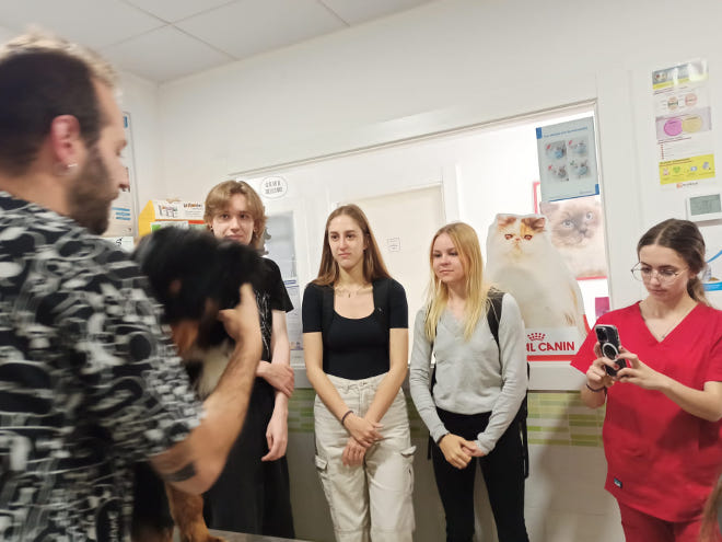 grupa uczniów w klinice słucha wykładu lekarza, który trzyma psa