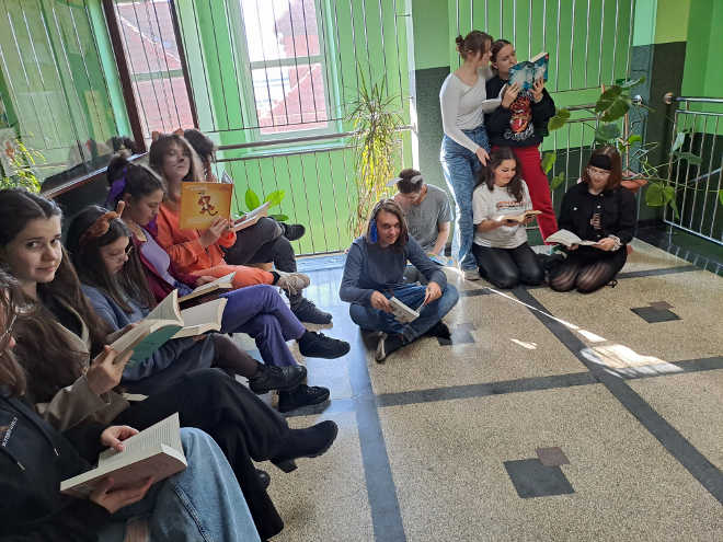 uczniowie na korytarzu szkolnym siedzą na ławce i czytają w czasie przerwy